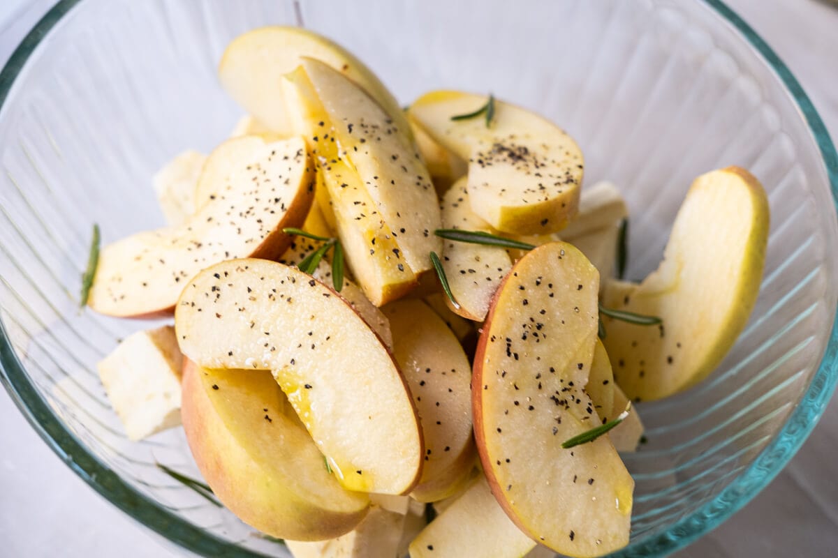 Apple slices, cubed sweet potatoes, olive oil, finely chopped and rosemary in a bowl. 