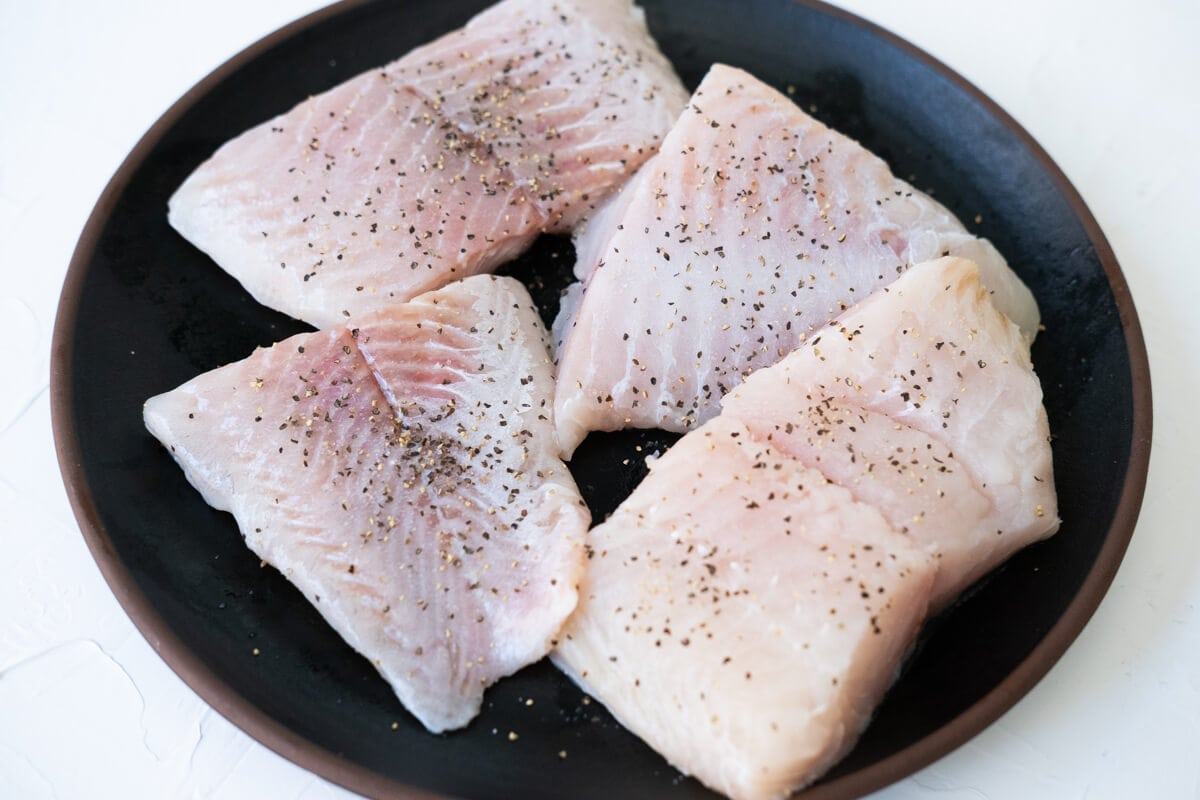 Catfish fillets seasoned with salt and pepper in a black plate.