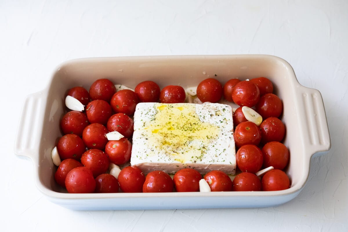 Cherry tomatoes arranged around feta cheese in the center in a baking dish. 