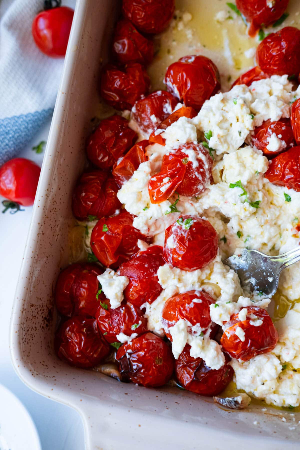 Burst juicy cherry tomato mixed with feta cheese scooped by a spoon in a baking dish. 