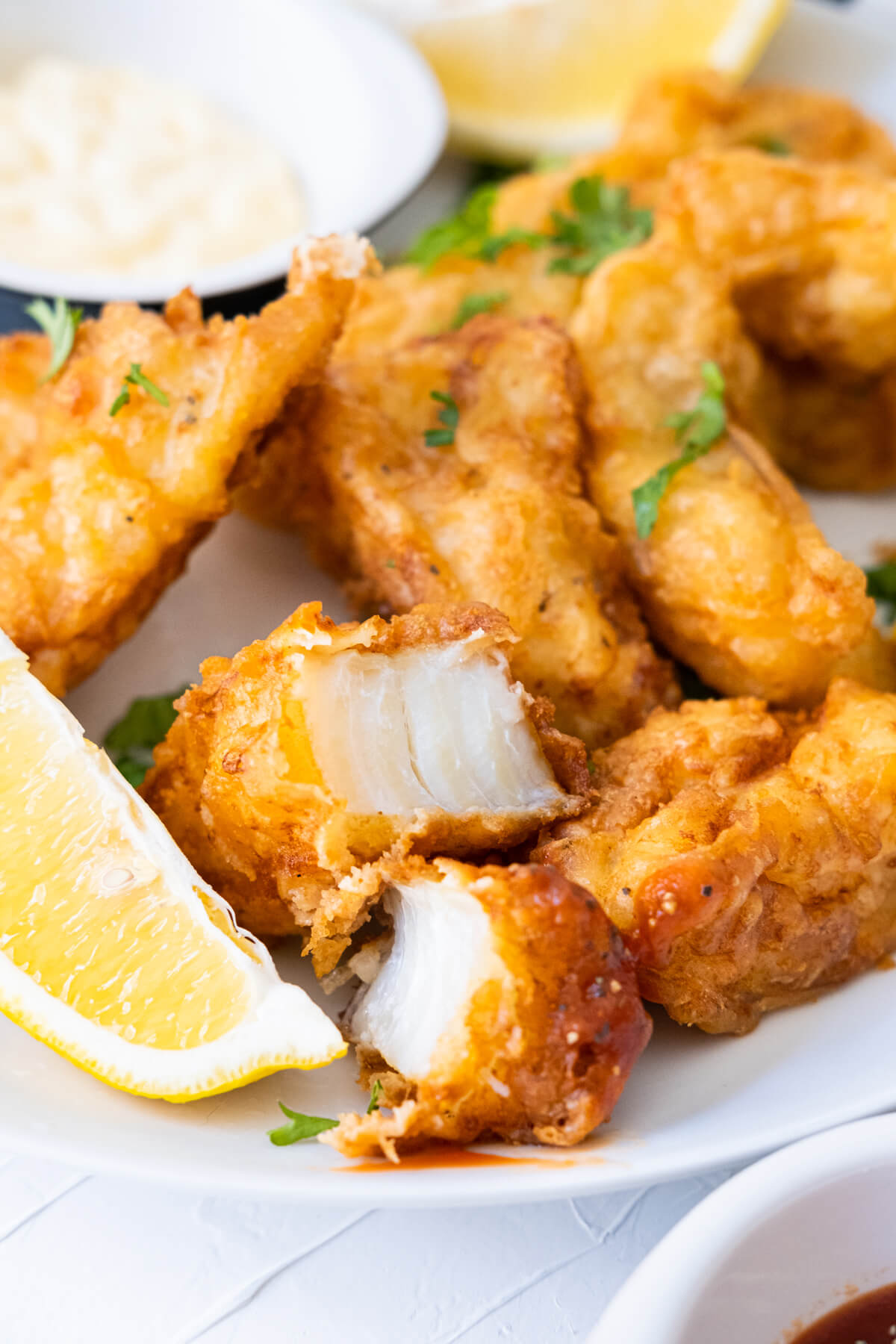 Pieces of tender, flaky beer-battered fish on a plate with lemon wedges and mayo. 