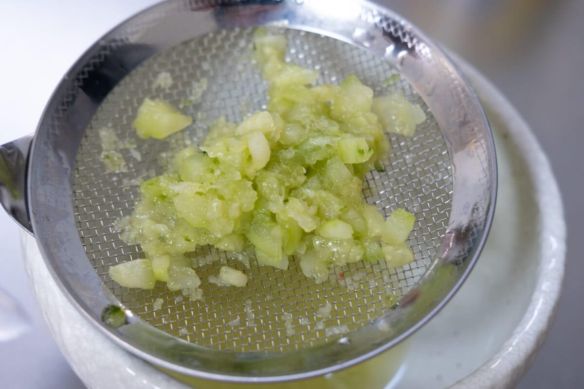 Grated cucumber sprinkled with salt on a strainer. 
