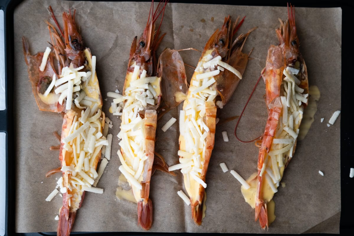 Prawns coated with mayonnaise mixture and stuffed with shredded cheese on a oven plate lined with baking paper. 