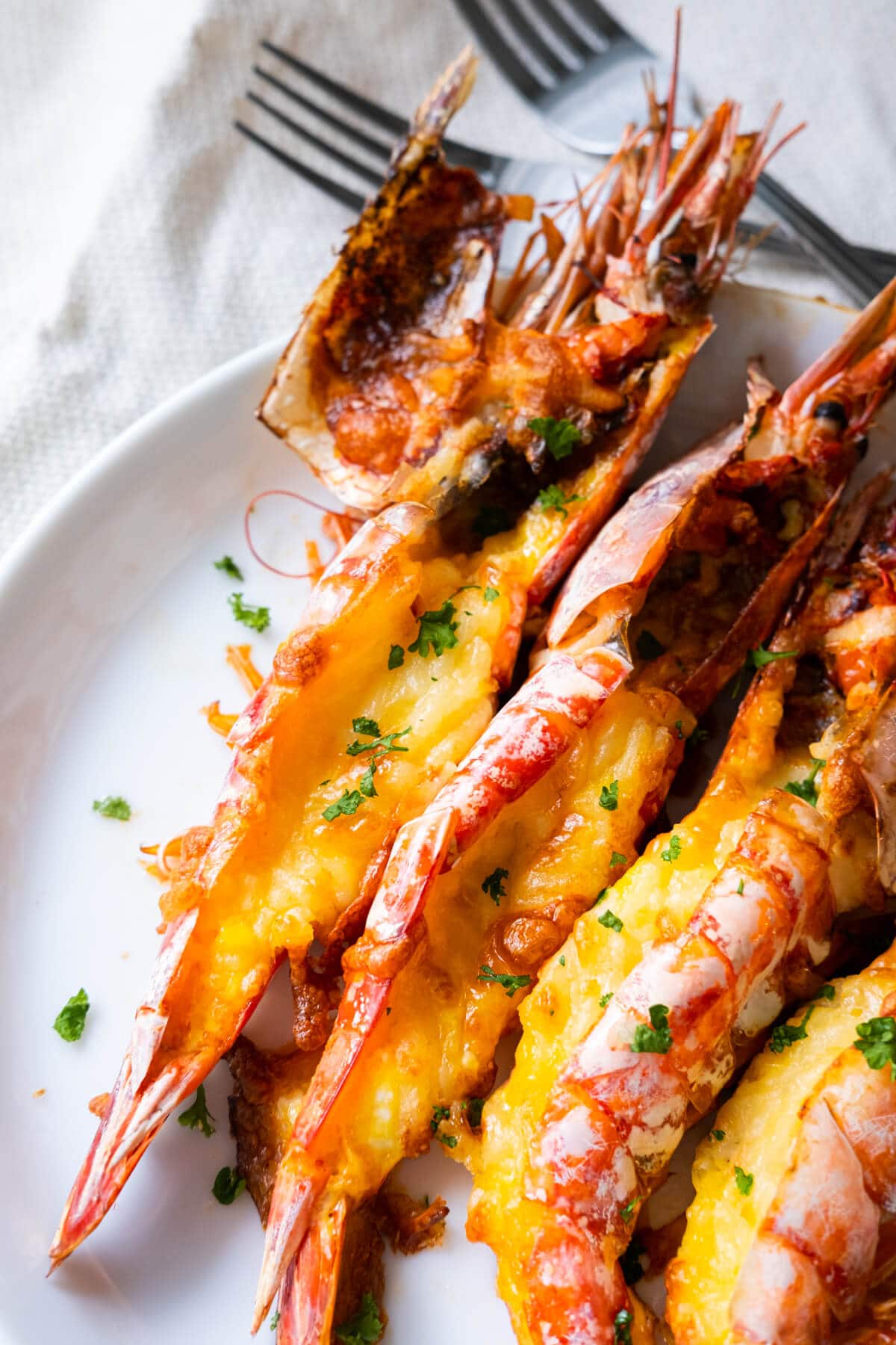 Close up shot of grilled prawns stuffed with baked cheese on a white shallow plate. 
