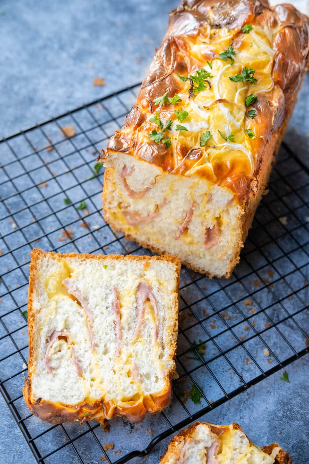 A loaf of bread with golden-brown crust and a savory filling of ham and melted cheese in between with one slice of it cut out.