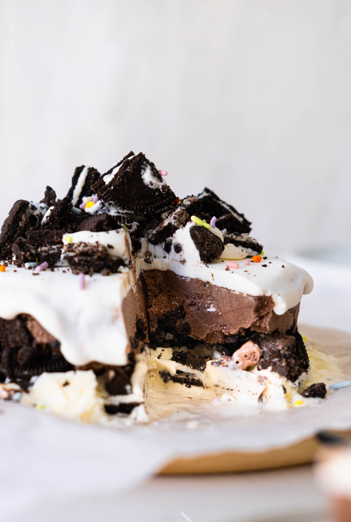 A cut section of cake with three layers: chocolate ice cream, Oreo crumbs and vanilla ice cream topped with Oreo chunks and rainbow sprinkles.  