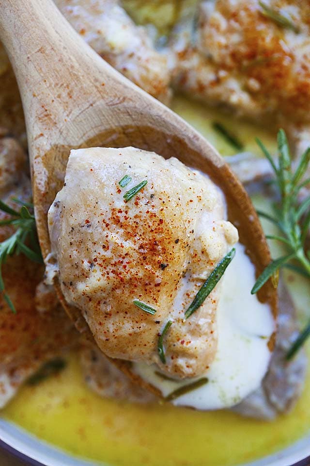 Top down picture of a boneless and skinless chicken thigh with creamy garlic sauce, served with a wooden spoon.