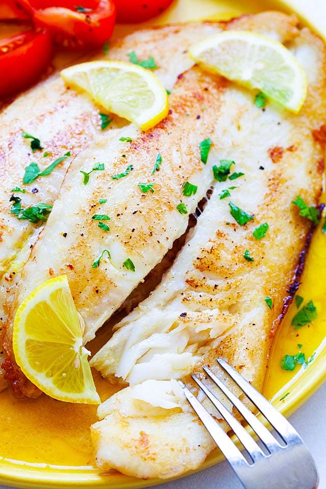 Pan fried fish with lemon butter sauce, served on a plate with a fork.