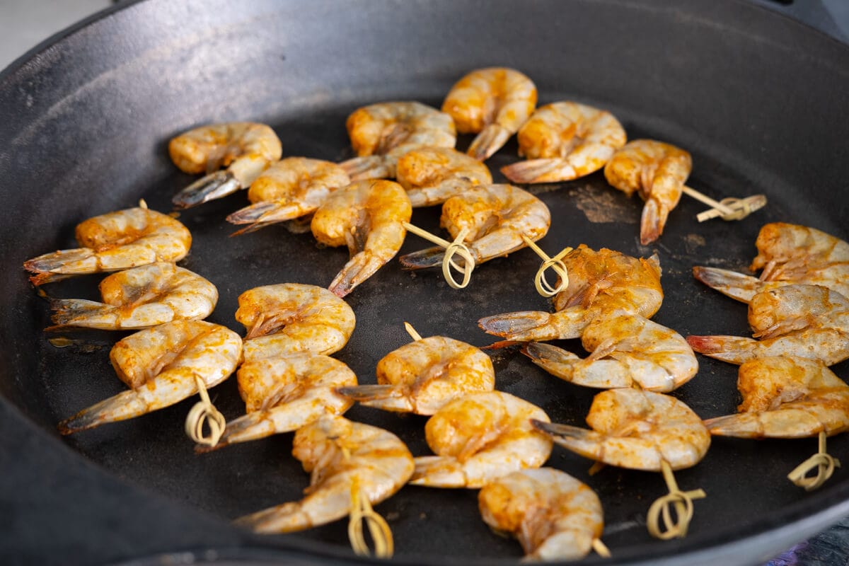 Shrimp skewers seasoned with Old Bay seasoning laid on cast iron pan. 