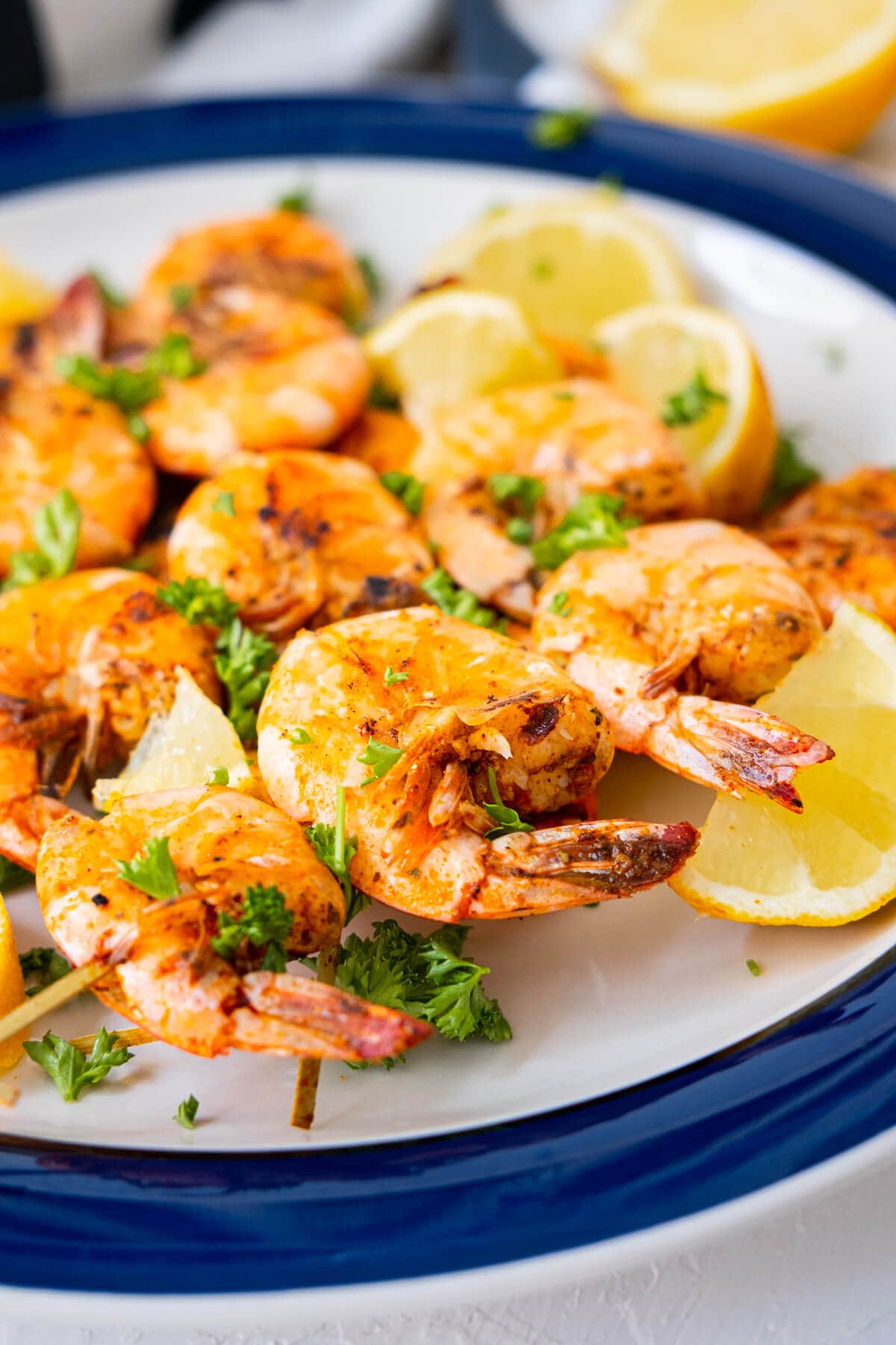 Crispy, grilled shrimp skewers seasoned with Old Bay seasoning on a plate served with lemon wedges. 