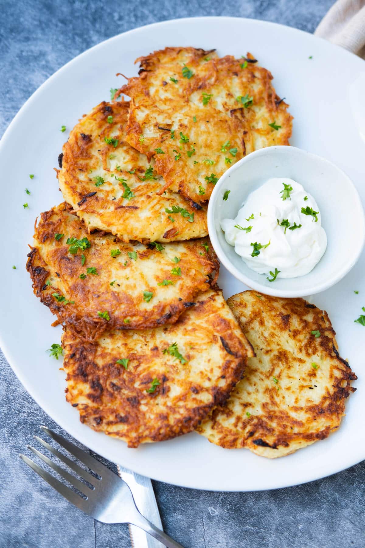 Potato pancakes served on a plate with a bowl of sour cream on the side. 
