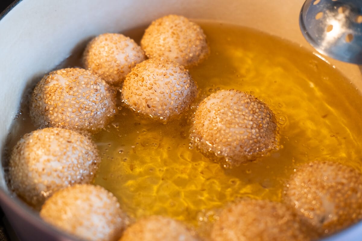 Sesame coated balls being deep fried in a heavy-bottom pot. 