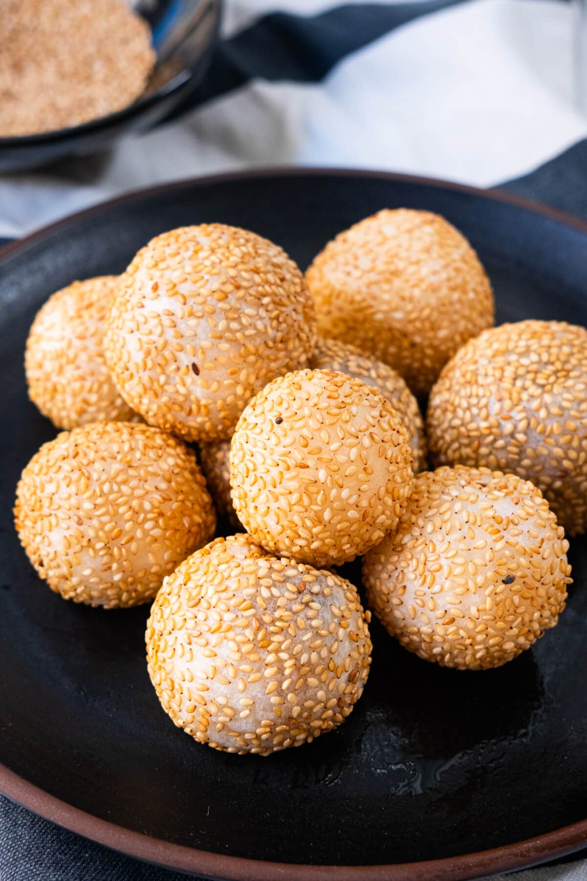 Golden sesame balls in a plate with sesame seeds on the side. 