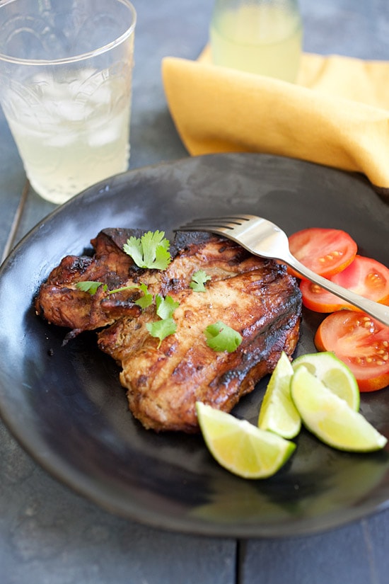 Juicy grilled pork chops served on a plate with sides of tomatoes and salad.